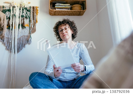 Beautiful intelligent curly haired female in her 40s with glasses reading book on bed, calm thoughtful mood, indoor routine, attractive confident woman, quiet lifestyle Beautiful intelligent curly haired female in her 40s with glasses reading book on bed, calm thoughtful mood, indoor routine, attractive confident woman, quiet lifestyle 138792036