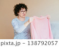 Middle aged woman holding pink sweater and inspecting result after using fabric shaver. Satisfied expression, clothing care, textile maintenance, everyday home routine, cozy interior. 138792057