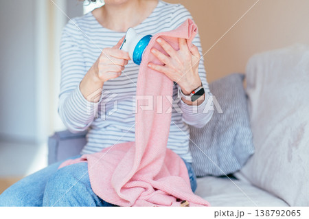 Close up female hands using electric fabric shaver on pink knitwear. Unrecognizable woman removing pills from textile, clothing care routine, home maintenance, soft fabric detail. Close up female hands using electric fabric shaver on pink knitwear. Unrecognizable woman removing pills from textile, clothing care routine, home maintenance, soft fabric detail. 138792065