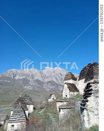 Dargavs necropolis, City of the Dead, North Ossetia, Russia. Rows of white stone tombs with pointed roofs against a backdrop of rugged Caucasus peaks 138792203