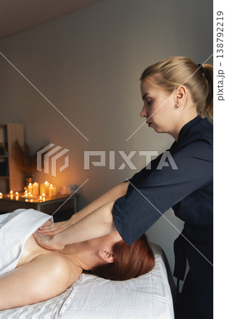 Woman lying on a massage table receiving a professional back and shoulder massage in a relaxing spa environment with candles Woman lying on a massage table receiving a professional back and shoulder massage in a relaxing spa environment with candles 138792219