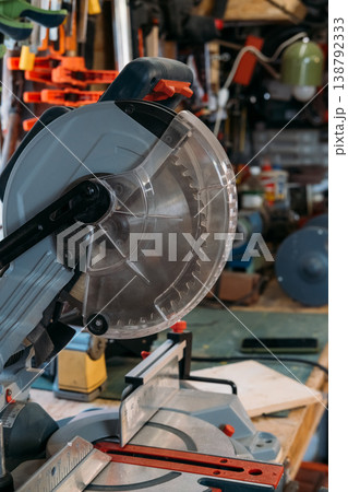 Miter saw. Circular blade. Sharp professional electric carpentry equipment with transparent plastic safety shield in workshop interior. 138792333