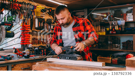 Woodworking process. Furniture making. Man polishing plank with handheld belt sander. Carpenter occupation with diy project workshop. 138792336