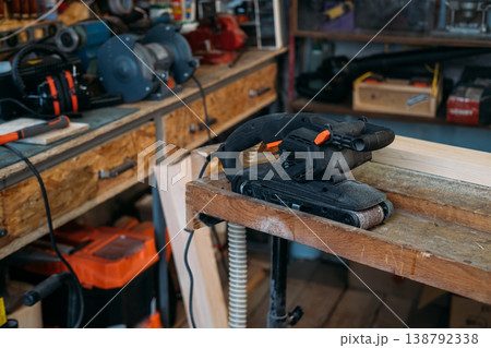 Carpentry equipment. Belt sander. Portable electric power joinery tool for woodworking near professional bench grinder in garage interior. Carpentry equipment. Belt sander. Portable electric power joinery tool for woodworking near professional bench grinder in garage interior. 138792338