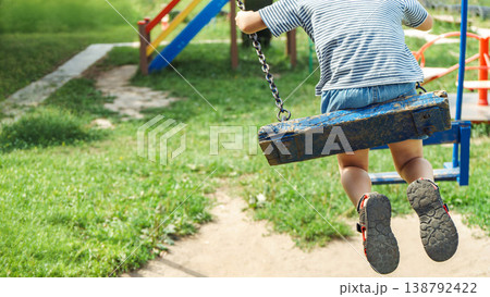 Boy captured in candid moment swinging as background features vibrant playground scene 138792422