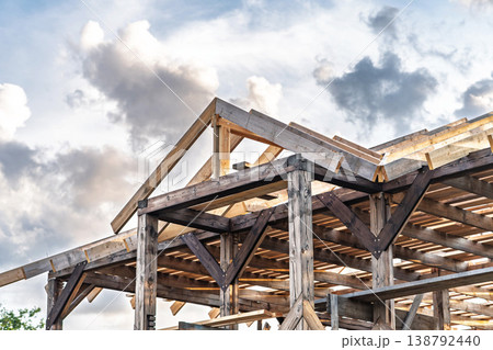 Wooden framework of an unfinished cottage roof in countryside setting with clouds sky Wooden framework of an unfinished cottage roof in countryside setting with clouds sky 138792440