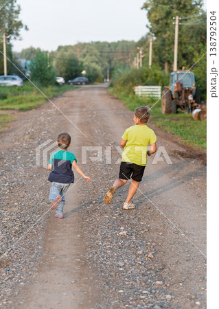 Two boys running on gravel road racing toward distant farmhouse under warm sunlight Two boys running on gravel road racing toward distant farmhouse under warm sunlight 138792504