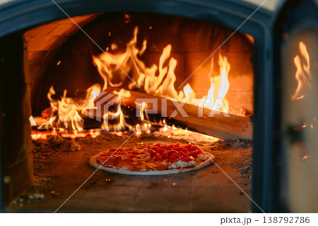 Pizza baking in traditional wood fired oven with bright flames and glowing embers. 138792786