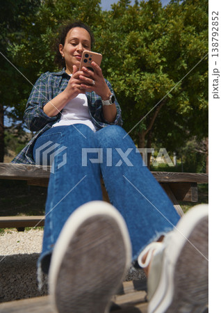 Low angle view of woman using smartphone outdoors against blue sky Low angle view of woman using smartphone outdoors against blue sky 138792852