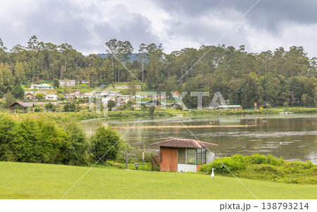 Tranquil Lakeside Village amidst Lush Green Hills and Overcast Sky, Serene Landscape with Rural Homes by Calm Water. Nuwara Eliya town in Sri Lanka. Tranquil Lakeside Village amidst Lush Green Hills and Overcast Sky, Serene Landscape with Rural Homes by Calm Water. Nuwara Eliya town in Sri Lanka. 138793214