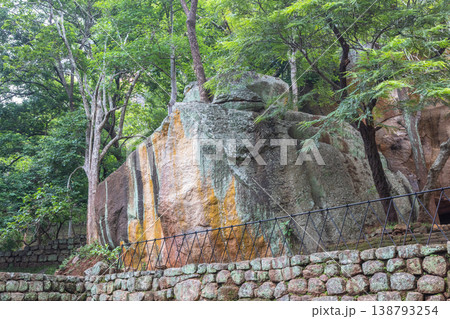 Sigiriya ancient rock fortress in Sri Lanka. Massive ancient rock formations and lush green trees compose a tranquil jungle scene with historic stone wall detail 138793254