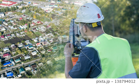 Surveyor in a hard hat and high-visibility vest uses a device Surveyor in a hard hat and high-visibility vest uses a device 138794012