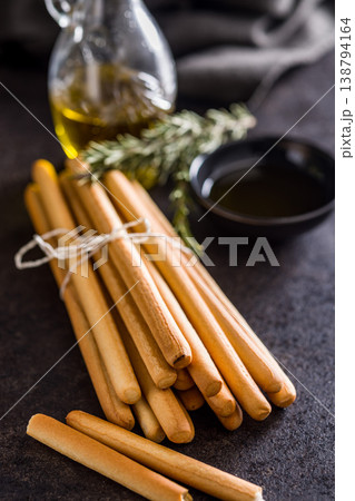 Bundled Italian Breadsticks (Grissini) with Olive Oil and Rosemary on Dark Surface Bundled Italian Breadsticks (Grissini) with Olive Oil and Rosemary on Dark Surface 138794164