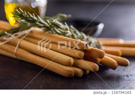 Bundled Italian Breadsticks (Grissini) with Olive Oil and Rosemary on Dark Surface Bundled Italian Breadsticks (Grissini) with Olive Oil and Rosemary on Dark Surface 138794165