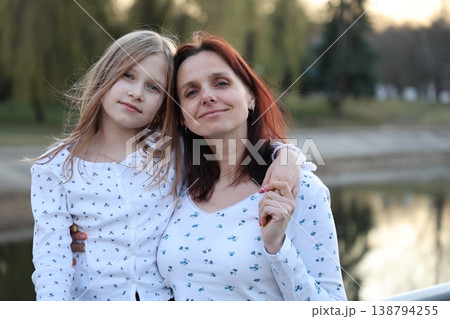 A brunette mother with her 9-year-old blonde daughter in light-colored sweaters outside in the spring. Happy beautiful family. 138794255