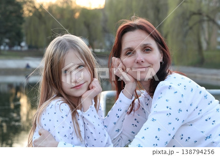 A brunette mother with her 9-year-old blonde daughter in light-colored sweaters outside in the spring. Happy beautiful family. 138794256