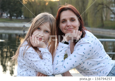 A brunette mother with her 9-year-old blonde daughter in light-colored sweaters outside in the spring. Happy beautiful family. 138794257