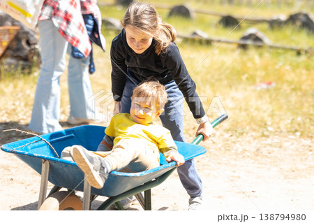 Big sister pushing little brother in wheelbarrow Big sister pushing little brother in wheelbarrow 138794980