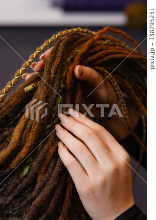 Hands braiding dreadlocks with decorative threads close up 138795251