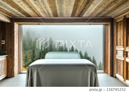 The interior of a treatment room in a modern chalet style, crafted entirely from light wood with a rich texture. A minimalist massage table covered with a soft gray sheet stands in the center of the 138795252