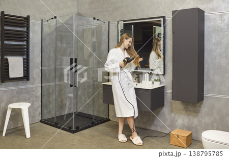 Beautiful young girl drying hair using hairdryer standing in modern bathroom interior. 138795785