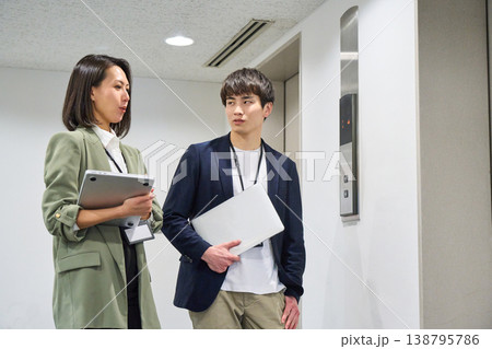 エレベーター前でPCを持ち、笑顔で立っている日本人男女ビジネス人物 エレベーター前でPCを持ち、笑顔で立っている日本人男女ビジネス人物 138795786
