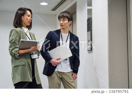 エレベーター前でPCを持ち、笑顔で立っている日本人男女ビジネス人物 エレベーター前でPCを持ち、笑顔で立っている日本人男女ビジネス人物 138795791