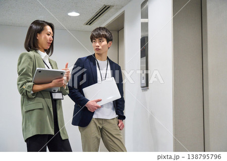 エレベーター前でPCを持ち、笑顔で立っている日本人男女ビジネス人物 エレベーター前でPCを持ち、笑顔で立っている日本人男女ビジネス人物 138795796