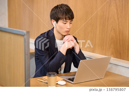 パーテーション席でイヤホンをしてPC作業に集中する男性社員 138795807