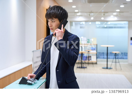 オフィスの受付で内線電話をかける若いビジネスマン 138796913