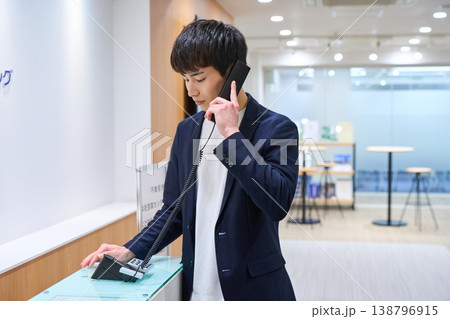 オフィスの受付で内線電話をかける若いビジネスマン オフィスの受付で内線電話をかける若いビジネスマン 138796915