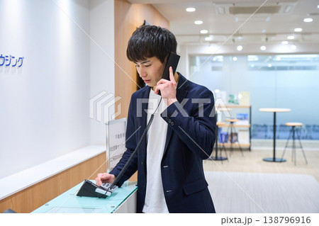 オフィスの受付で内線電話をかける若いビジネスマン 138796916