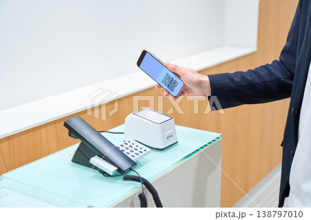 オフィスの無人受付でスマートフォンのQRコードをかざすビジネスマンの手元 138797010