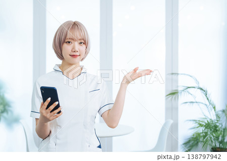 スマホを持って案内するハイトーンヘアの女性スタッフ スマホを持って案内するハイトーンヘアの女性スタッフ 138797942