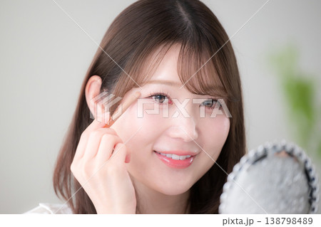 手鏡を見ながらアイシャドウを塗る女性のナチュラルメイクと美容ケアイメージクローズアップ	 138798489