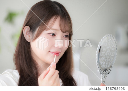 手鏡を見ながらリップを塗る女性のナチュラルメイクと美容ケア リップグロスや唇のケアなどのイメージ 手鏡を見ながらリップを塗る女性のナチュラルメイクと美容ケア リップグロスや唇のケアなどのイメージ 138798498