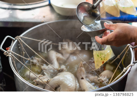Clear chicken soup from chicken rice stall ladled into plastic bag from large pot simple street food serving with herbs and light broth in local market Clear chicken soup from chicken rice stall ladled into plastic bag from large pot simple street food serving with herbs and light broth in local market 138798825