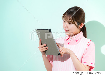 グリーン背景で介護士や保育士として働く女性の訪問介護の仕事など、タブレットを指差して持つit化 グリーン背景で介護士や保育士として働く女性の訪問介護の仕事など、タブレットを指差して持つit化 138798988