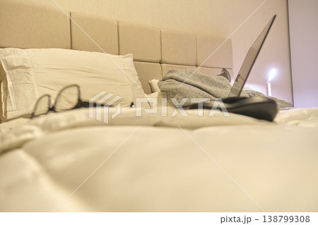 Laptop and glasses resting on bed surface 138799308