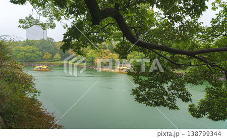 Osaka, Japan - Sep 22 2024, panoramic view of the moat around Osaka Castle on which a yellow tourist boat floats, view from the bridge through foliage and a tree branch, on a rainy day, Osaka, Japan 138799344