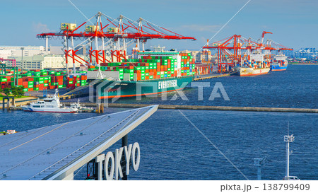 Tokyo, Japan - Oct 2 2024, panoramic view of docks with cranes and a moored giant cargo ship loaded with containers, in foreground is signage with word Tokyo on roof of Tokyo cruise port, Tokyo, Japan Tokyo, Japan - Oct 2 2024, panoramic view of docks with cranes and a moored giant cargo ship loaded with containers, in foreground is signage with word Tokyo on roof of Tokyo cruise port, Tokyo, Japan 138799409