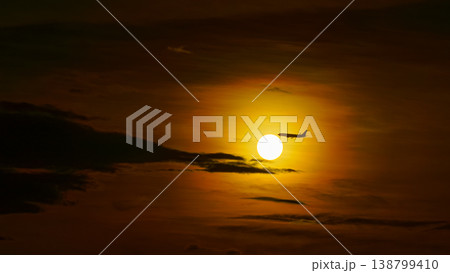 Tokyo, Japan - Oct 2 2024, Panoramic view of the bright orange sunset sun among dark clouds, silhouette of an airplane flies past the sun, Tokyo, Japan Tokyo, Japan - Oct 2 2024, Panoramic view of the bright orange sunset sun among dark clouds, silhouette of an airplane flies past the sun, Tokyo, Japan 138799410
