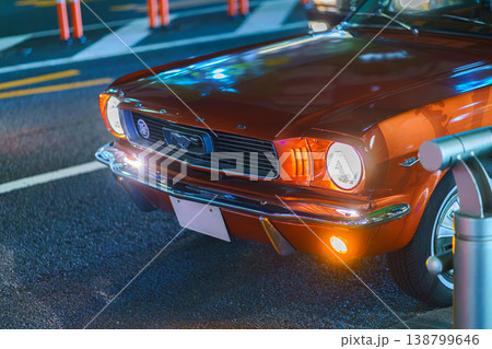 Tokyo, Japan - Oct 15 2024, Close-up view of the front bumper hood and burning headlights of a retro Ford Mustang, on one of the roads of Tokyo, at nighttime, Tokyo, Japan 138799646