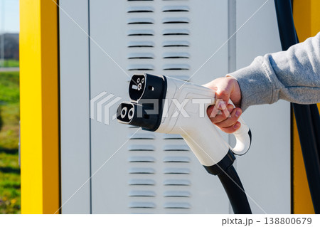 Electric car charger being held at a charging station in bright daylight Electric car charger being held at a charging station in bright daylight 138800679
