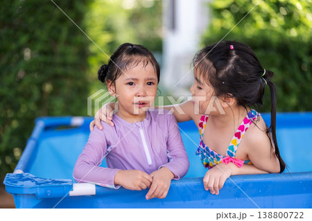 older sister comforting and hugging her crying child girl in portable swimming pool 138800722