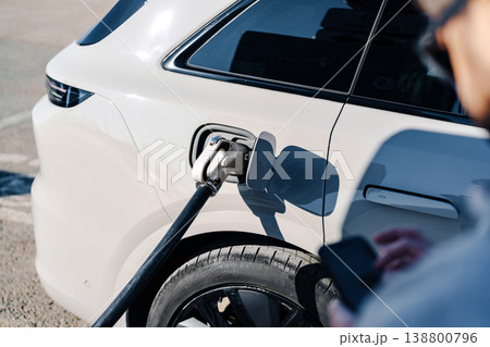 Electric car charger in use at a parking area during daytime hours Electric car charger in use at a parking area during daytime hours 138800796