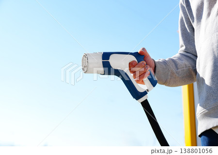 Electric car charger held by a person in a clear blue sky during daytime Electric car charger held by a person in a clear blue sky during daytime 138801056