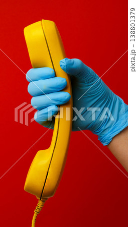 Holding a yellow phone with blue gloves in a red setting during a health crisis 138801379