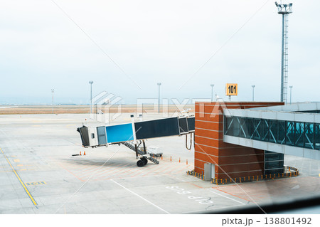 Plane boarding bridge is parked at gate 101 in an airport during a cloudy day Plane boarding bridge is parked at gate 101 in an airport during a cloudy day 138801492