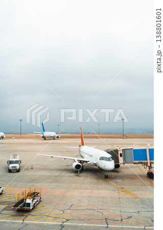 Planes parked at an airport during a cloudy day with ground service vehicles nearby Planes parked at an airport during a cloudy day with ground service vehicles nearby 138801601